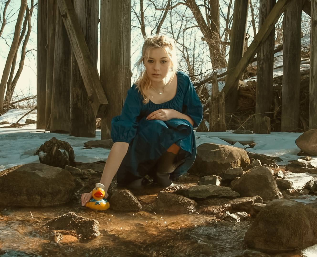 A beautiful model by a creek in front of a bridge